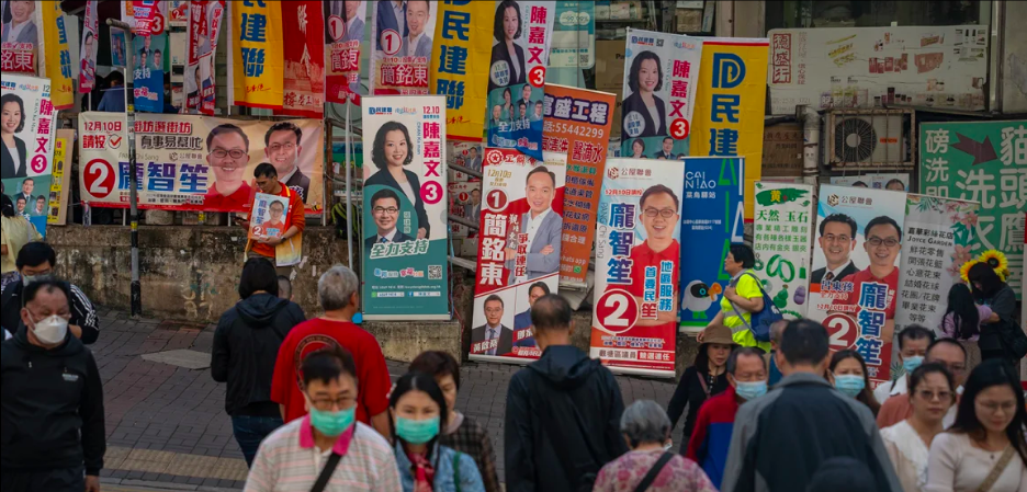 Des habitants traversent la rue devant un mur de banderoles de campagne pour les élections des conseils de district à Hong Kong, le 10 décembre 2023. Vernon Yuen/NurPhoto/Getty Images